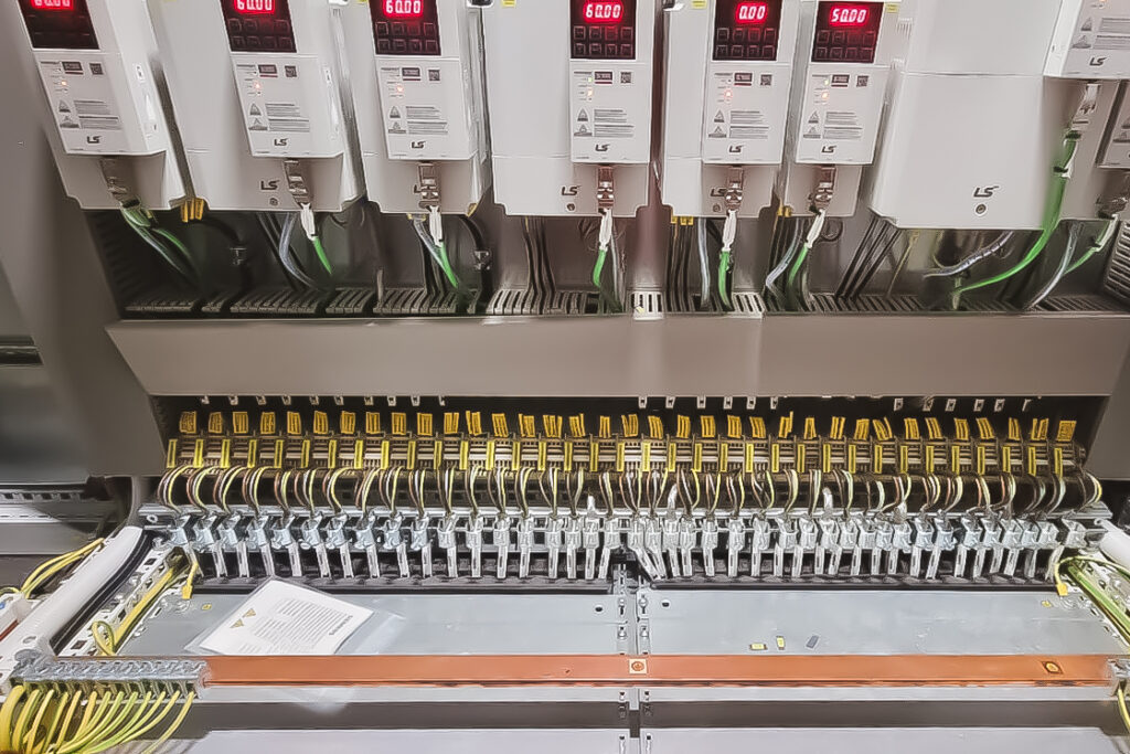 Szafa sterownicza z zainstalowanymi falownikami LS Electric, prezentująca wyraźnie oznakowane przewody zasilające i sterownicze w ramach systemu automatyki dla fabryki paszy.